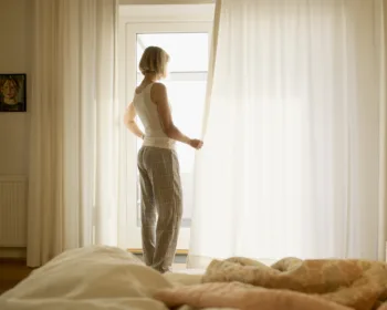Mature woman wearing pyjamas opening bedroom curtains
